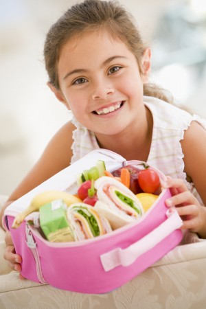 Young girl holding packed lunch in living room smiling